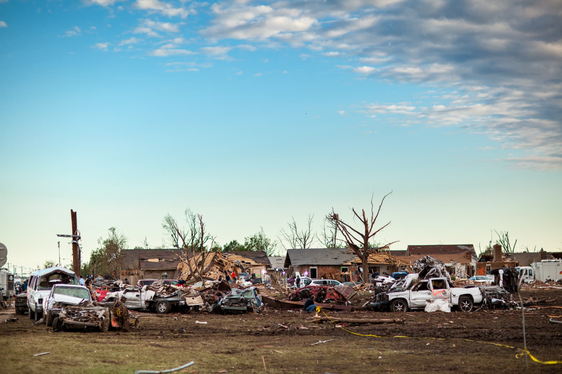 Neighborhood damaged by a tornado, with destroyed homes and vehicles under an open sky